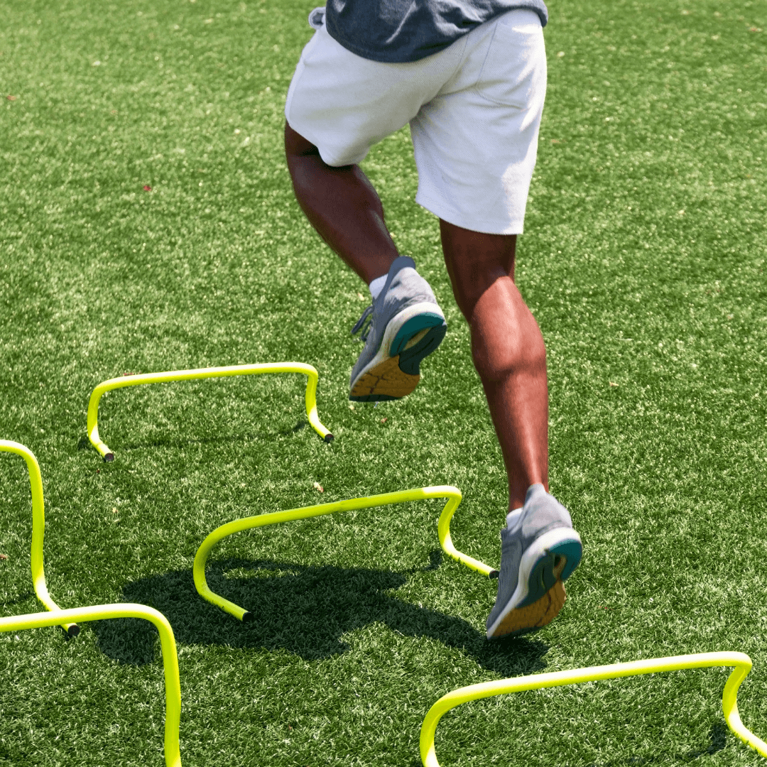 A young athlete runs through agility hurdles on a green field, demonstrating dynamic athletic training services.